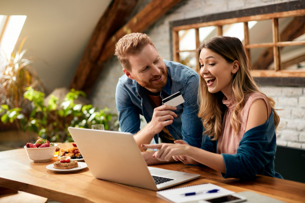 Happy woman pointing on something on laptop screen while shopping on the internet with her husband at home.